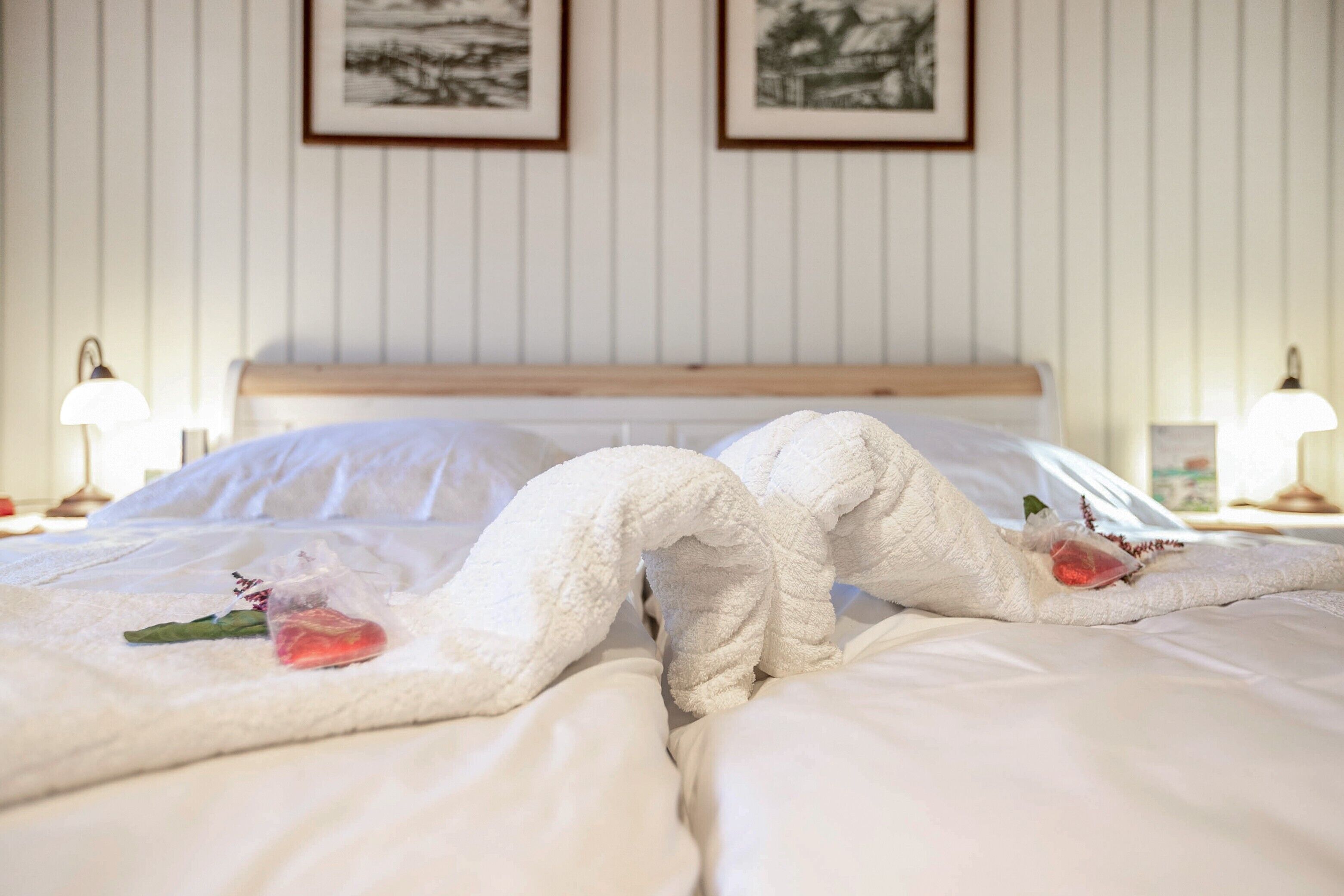A neatly made bed with white linens, a wooden headboard, and two bedside lamps.