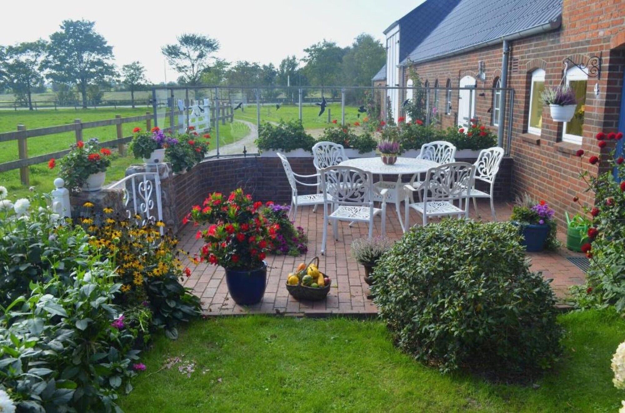 A patio with white chairs and a table, surrounded by potted plants and flowers.