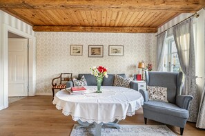 Huoneessa on pyöreä pöytä, sohva, tuoli, puinen katto ja seinillä on kehystettyjä tauluja.