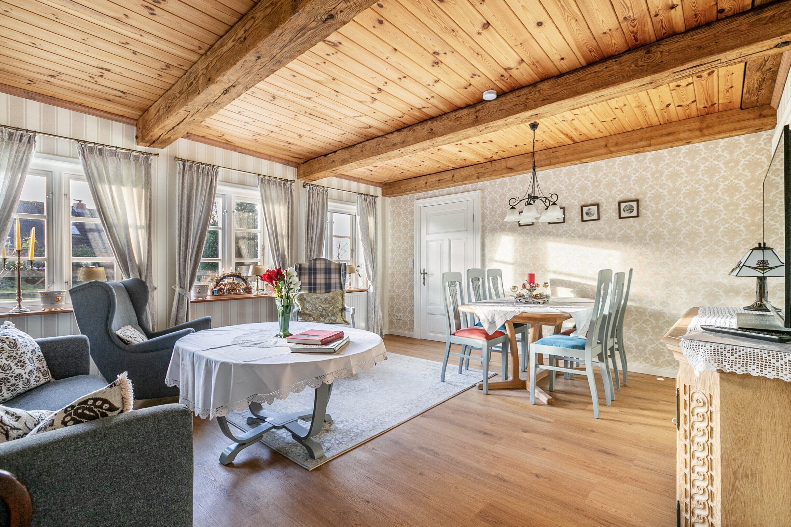 A cozy room with a wooden ceiling, a dining table with chairs, a sofa, and a window with curtains.