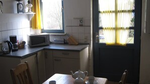 Una cocina con microondas, hervidor de agua y tetera sobre la encimera, una ventana con cortinas y una puerta con vistas al exterior.