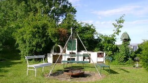 Un espacio al aire libre con césped, un columpio, un banco y una pequeña construcción con chimenea.