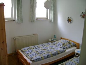 A bedroom with a bed, a radiator, a window with curtains, a small table, and a wall decoration.