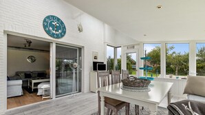 Un salon moderne avec un mur en briques blanches, une grande fenêtre et un coin repas comprenant une table et des chaises blanches.