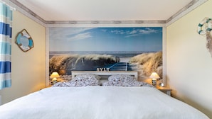 Une chambre avec un grand lit, une fresque murale représentant une plage et une enseigne « SYLT » au-dessus du lit.