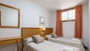 A hotel room with two beds, a wooden nightstand, a desk, and a window with curtains. - Las Floritas 4 (Playa de Las Americas)
