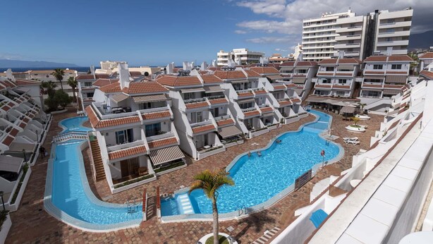 A resort with a large swimming pool, multiple balconies, and a view of the sea. - Las Floritas 4 (Playa de Las Americas)