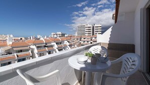 A balcony with white plastic chairs and a small round table, overlooking a cityscape with terracotta-tiled buildings and a clear blue sky. - Las Floritas 4 (Playa de Las Americas)