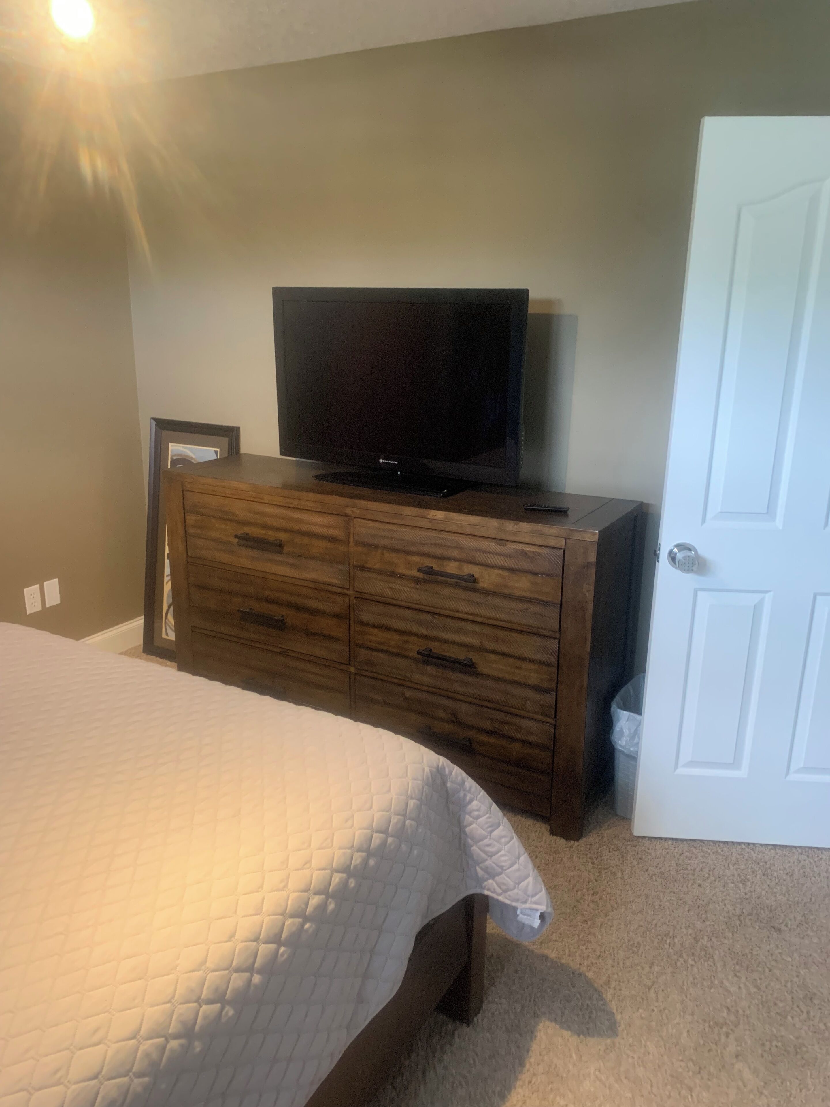 A bedroom with a bed, a dresser, a television, and a door.