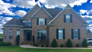 A two-story brick house with a gabled roof, multiple windows, and a well-maintained lawn.
