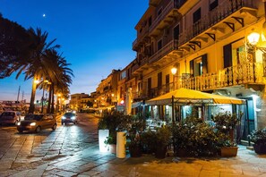 A street with buildings, cars, and outdoor seating areas with umbrellas. - The Blue Whale (La Maddalena)