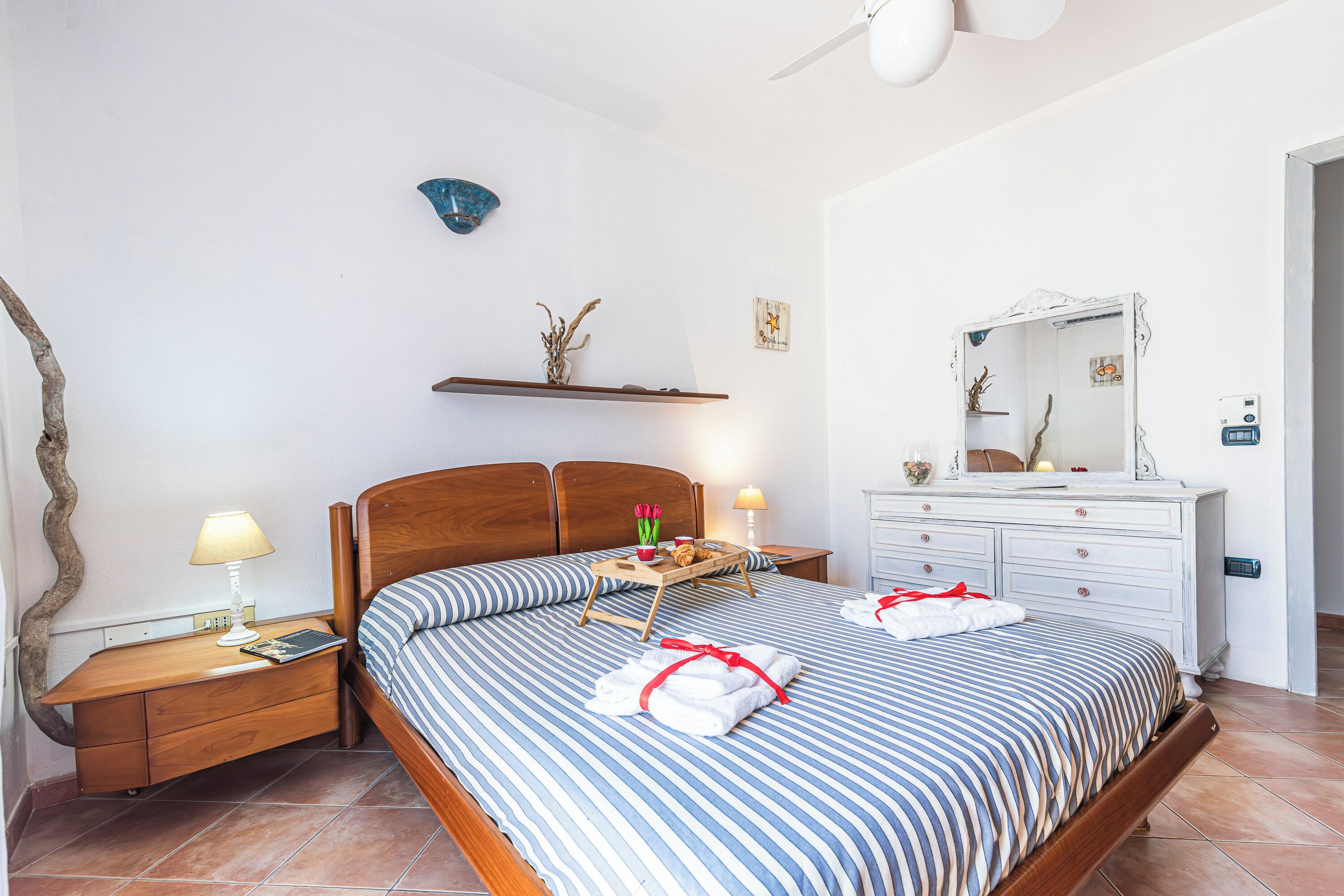 A neatly arranged bedroom with a bed, bedside tables, a dresser, and a mirror.