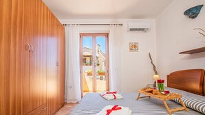 A bedroom with a wooden wardrobe, a bed with striped bedding, a breakfast tray with croissants, and a view of a courtyard through a glass door. - The Blue Whale (La Maddalena)