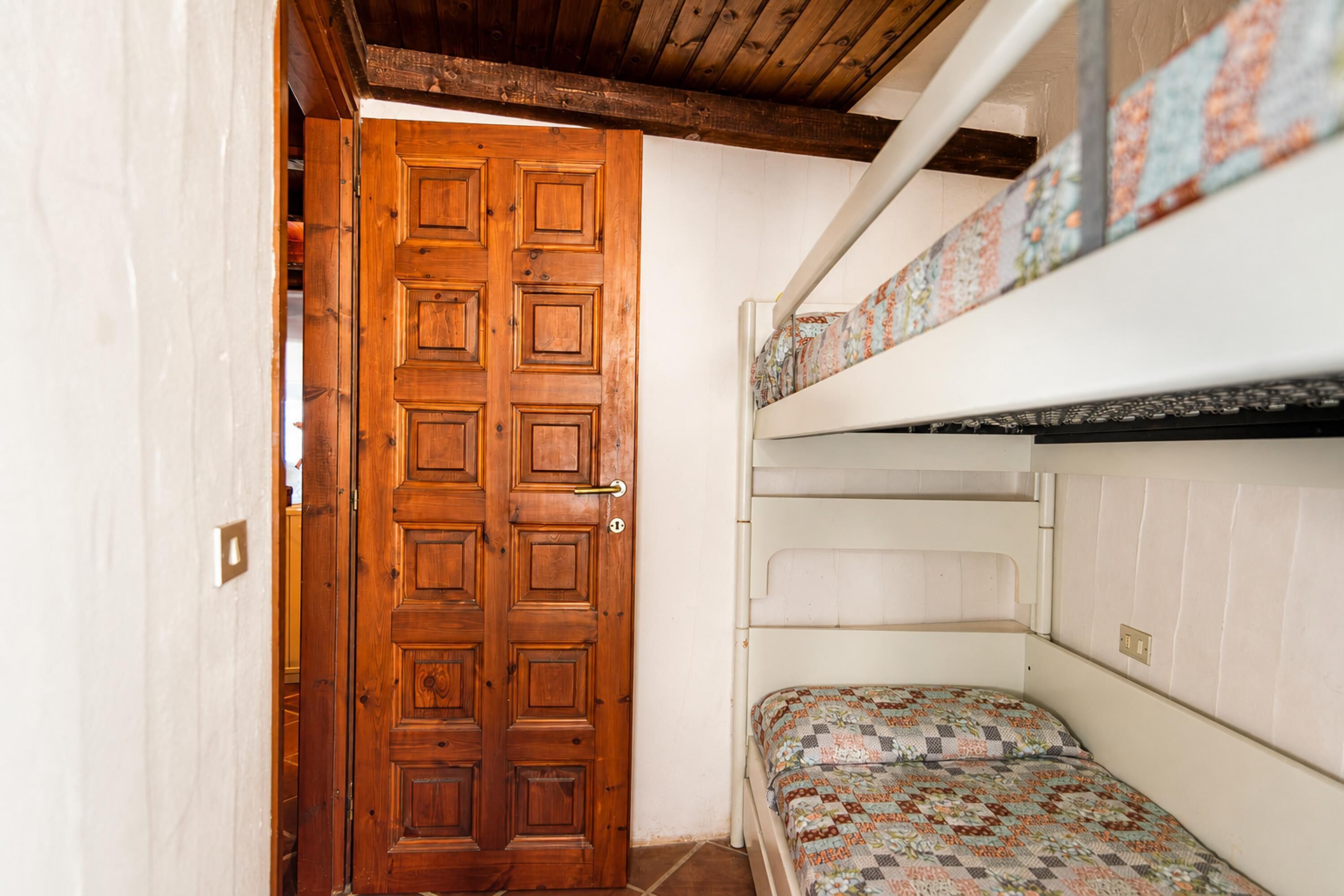 A room with a wooden door, bunk beds, and a patterned bedspread.