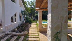 En sti der fører til et poolområde med en stenvæg og et træbeklædt pergola.