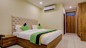 A bedroom with a tufted headboard, a bed with white bedding and colorful pillows, a bedside table with a phone, and an air conditioning unit on the wall. - Royal Culture (Greater Noida)