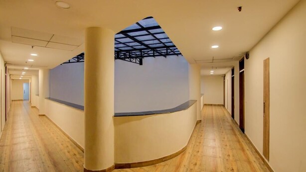 A hotel corridor with a skylight, wooden flooring, and a curved reception desk. - Royal Culture (Greater Noida)
