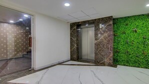 A lobby with a marble floor, a green wall with foliage, an elevator, and a patterned wall. - Royal Culture (Greater Noida)