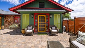 Une maison avec un toit rouge, des murs verts et une porte d’entrée jaune. On y trouve deux chaises en osier avec des coussins à l’extérieur.