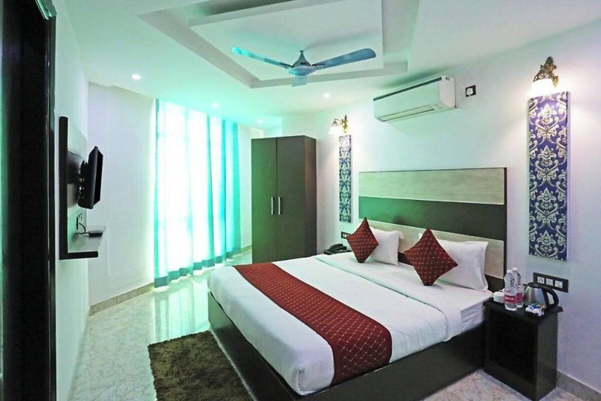 Una habitación de hotel moderna con una cama grande, un ventilador de techo, un equipo de aire acondicionado y una mesita de noche con un teléfono y una botella.