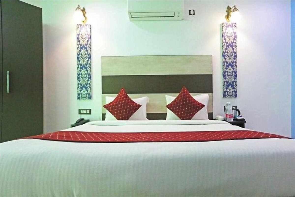 Una habitación de hotel con una cama grande, dos lámparas de pared, un aire acondicionado y una mesita de noche con un teléfono y una botella.