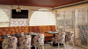 Un restaurante con techo de paneles de madera, un amplio banco acolchado, sillas con estampado floral y un separador decorativo.