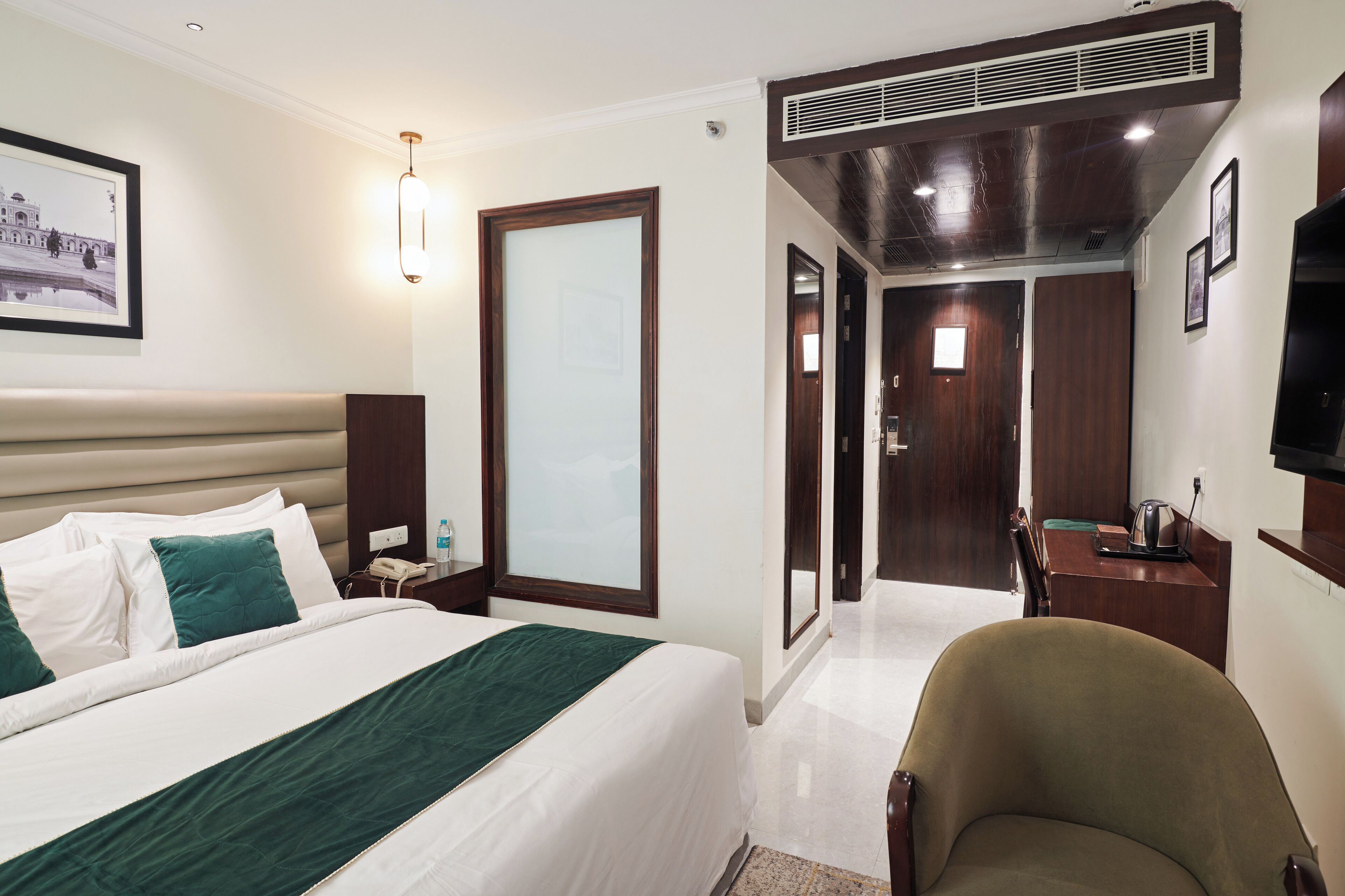 A hotel room with a bed, a desk, a chair, a television, and a bathroom visible through an open door.