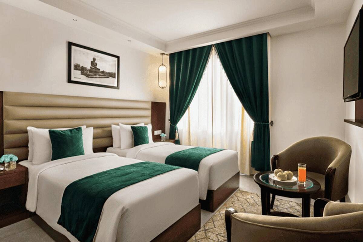 Quarto de hotel com duas camas, televisão, uma cadeira e uma pequena mesa com uma bebida.