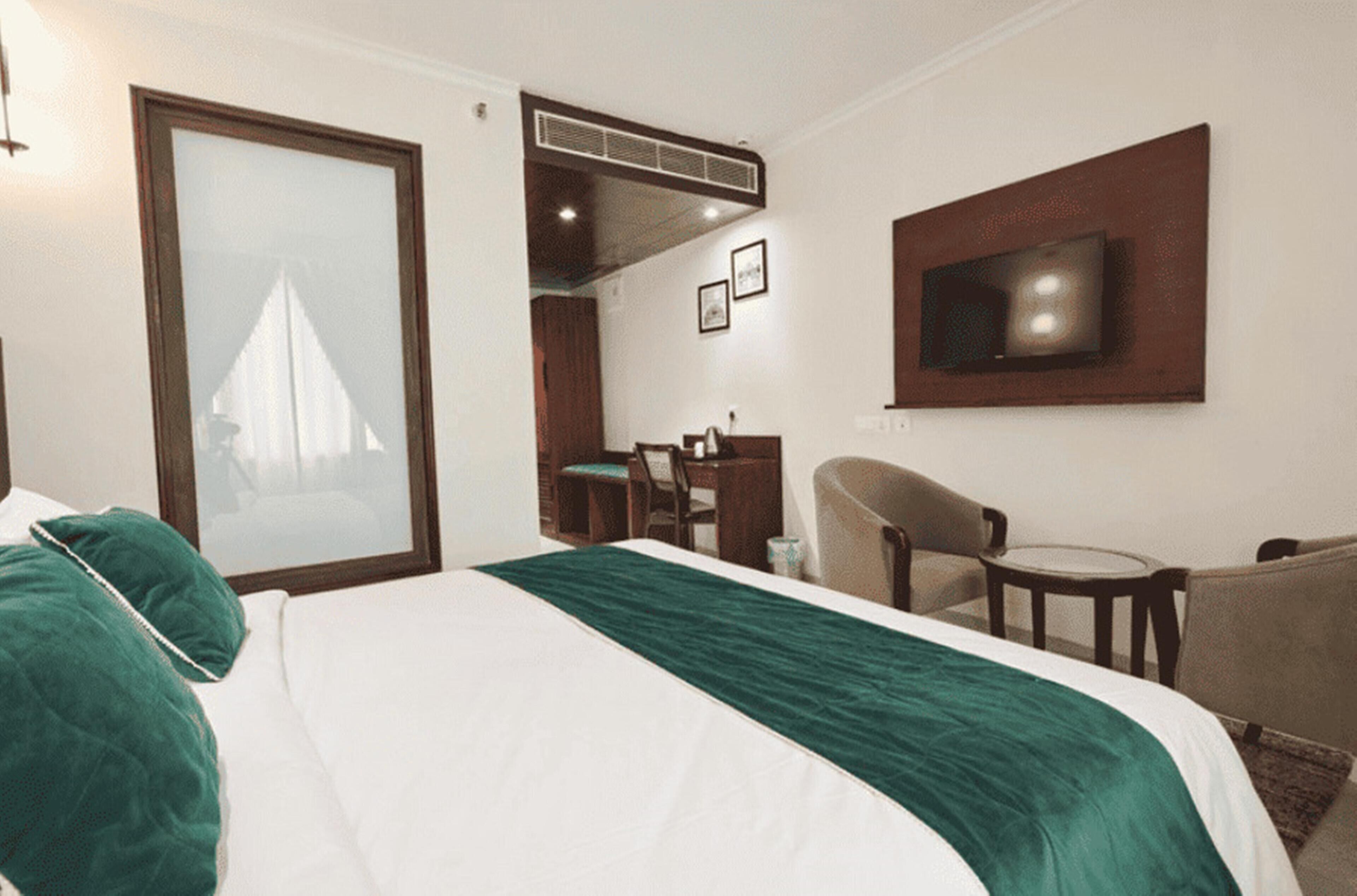 A hotel room with a bed, a TV mounted on the wall, a desk, and a chair.
