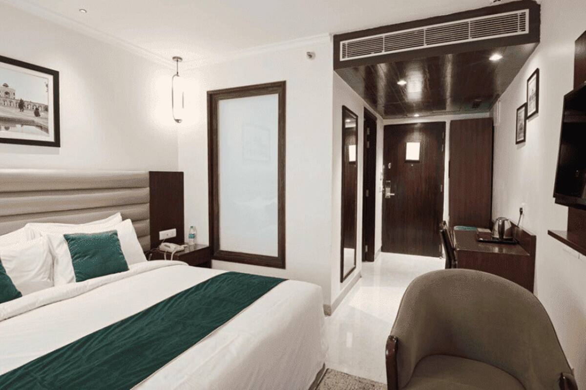 Quarto de hotel com uma cama, uma cadeira, uma mesa, televisão e porta que dá para um banheiro.