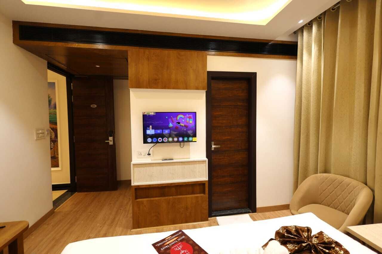 A hotel room with a TV mounted on a wooden shelf, a bed, a chair, and a door.