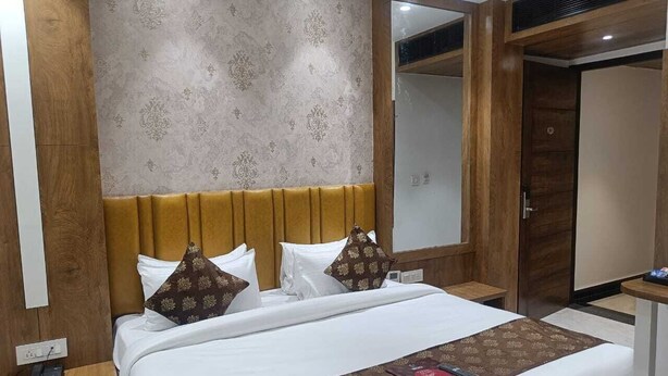 A hotel room with a large bed, wooden headboard, patterned wallpaper, a mirror, and a bedside table. - Tango Traxx (Amritsar)
