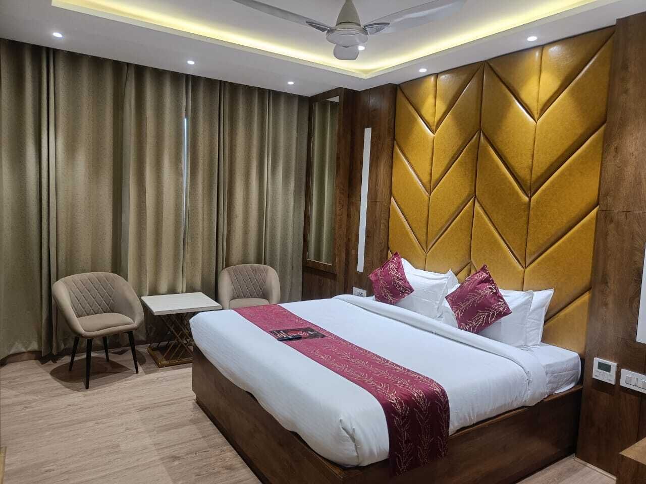 A hotel room with a large bed, two chairs, a small table, and a modern ceiling fan.