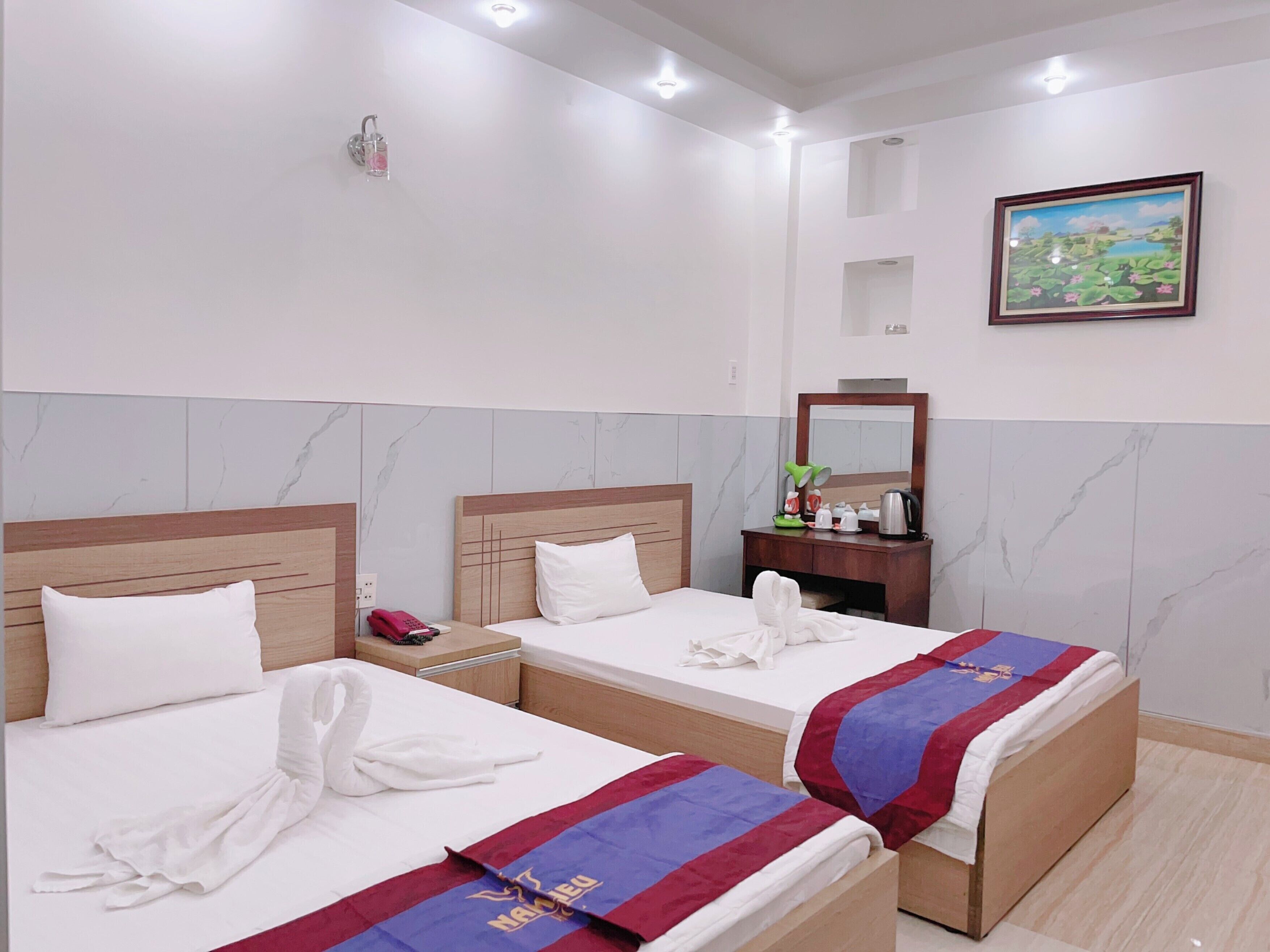 A hotel room with two beds, a bedside table with a phone, a mirror, and a painting on the wall.