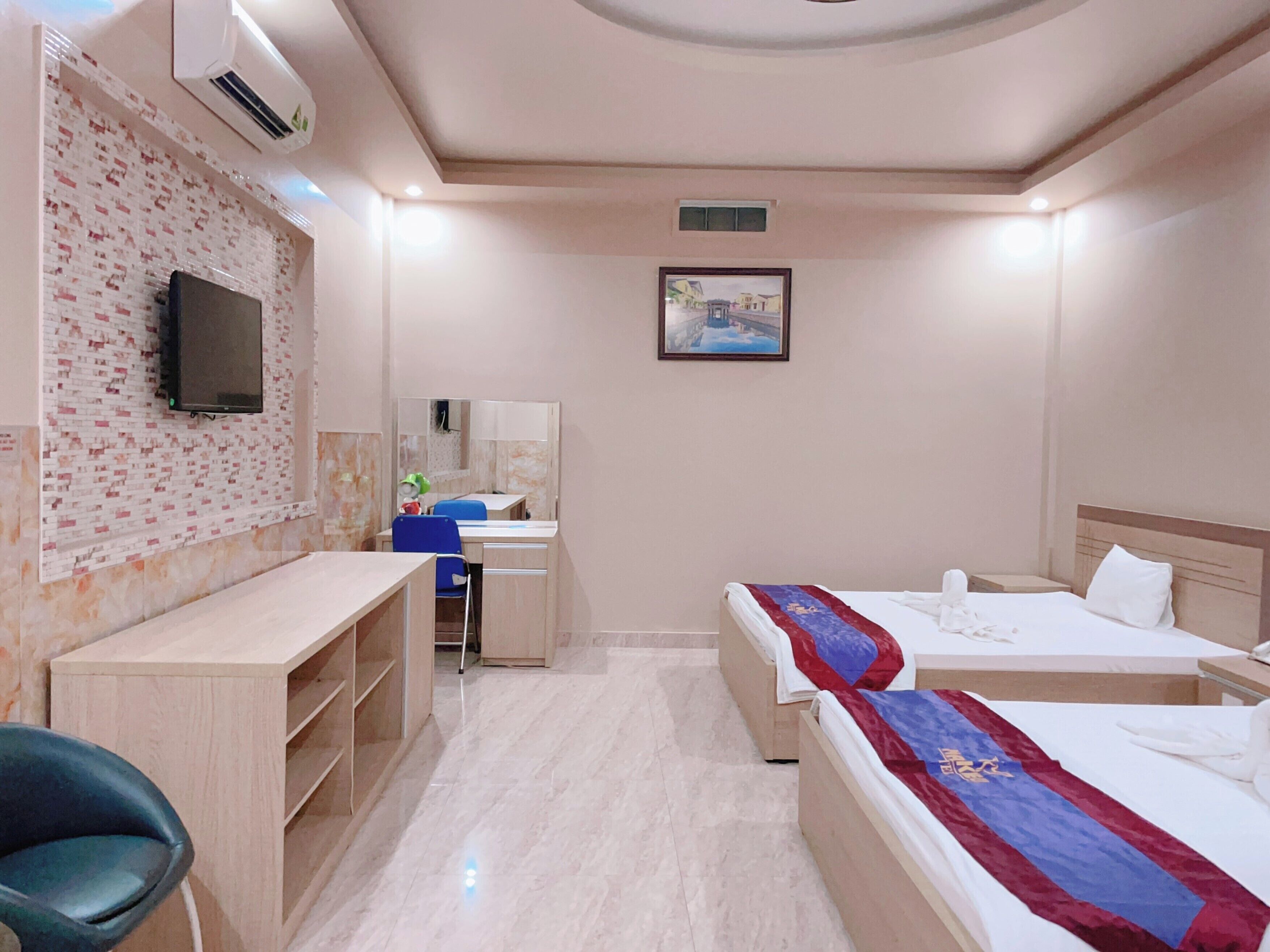 A hotel room with a desk, two beds, a TV, a painting, and a mirror.