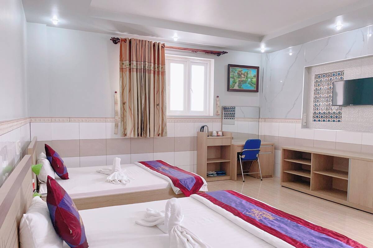 Habitación de hotel con dos camas, un escritorio, una silla, un televisor y un ventanal con cortinas.