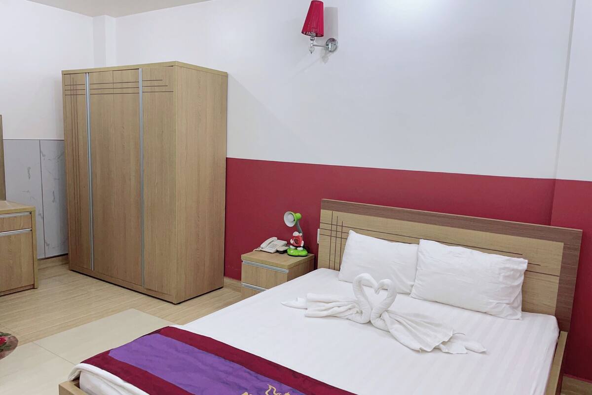 Una habitación de hotel con una cama, un armario, una mesita de noche y una pared roja.