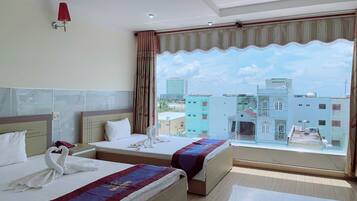 A hotel room with two beds, a large window with a city view, a red wall lamp, and a ceiling light.