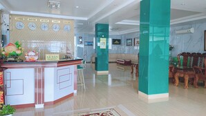 Un espace d’accueil comprenant un comptoir de réception, des horloges indiquant l’heure dans différentes villes, un panneau d’identification de la réception, ainsi qu’un coin salon avec des chaises et un canapé.