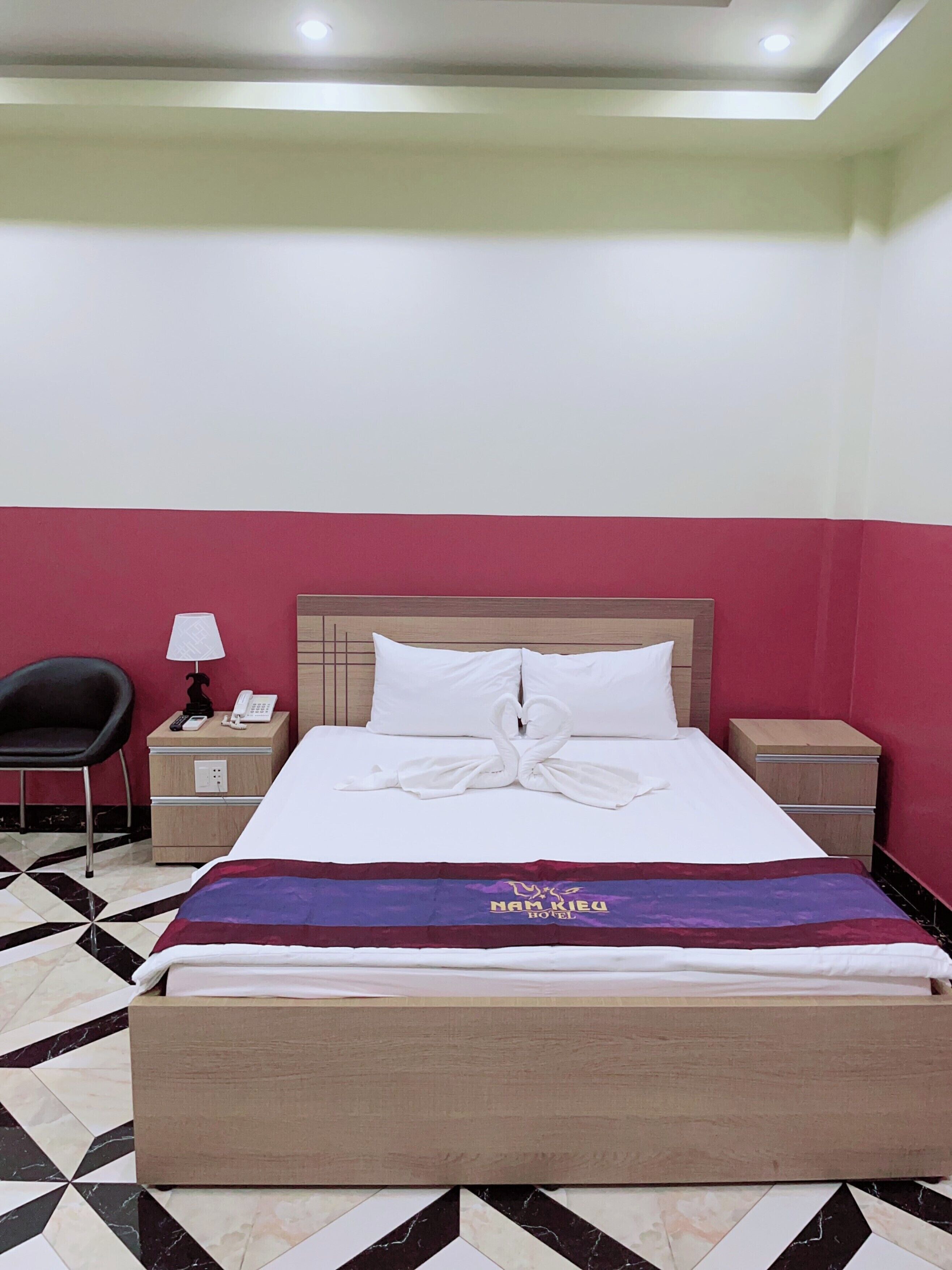 A hotel room with a bed, a nightstand, a chair, and a tiled floor.
