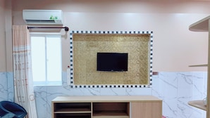 Une pièce avec un téléviseur fixé au mur, un meuble de rangement en bois en dessous, une fenêtre avec des rideaux et un sol carrelé.