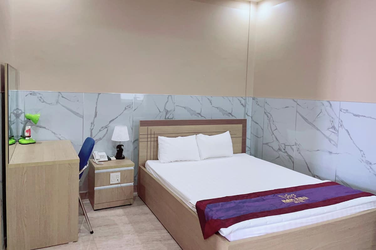 Una habitación de hotel con cama, escritorio, silla, lámpara y teléfono.