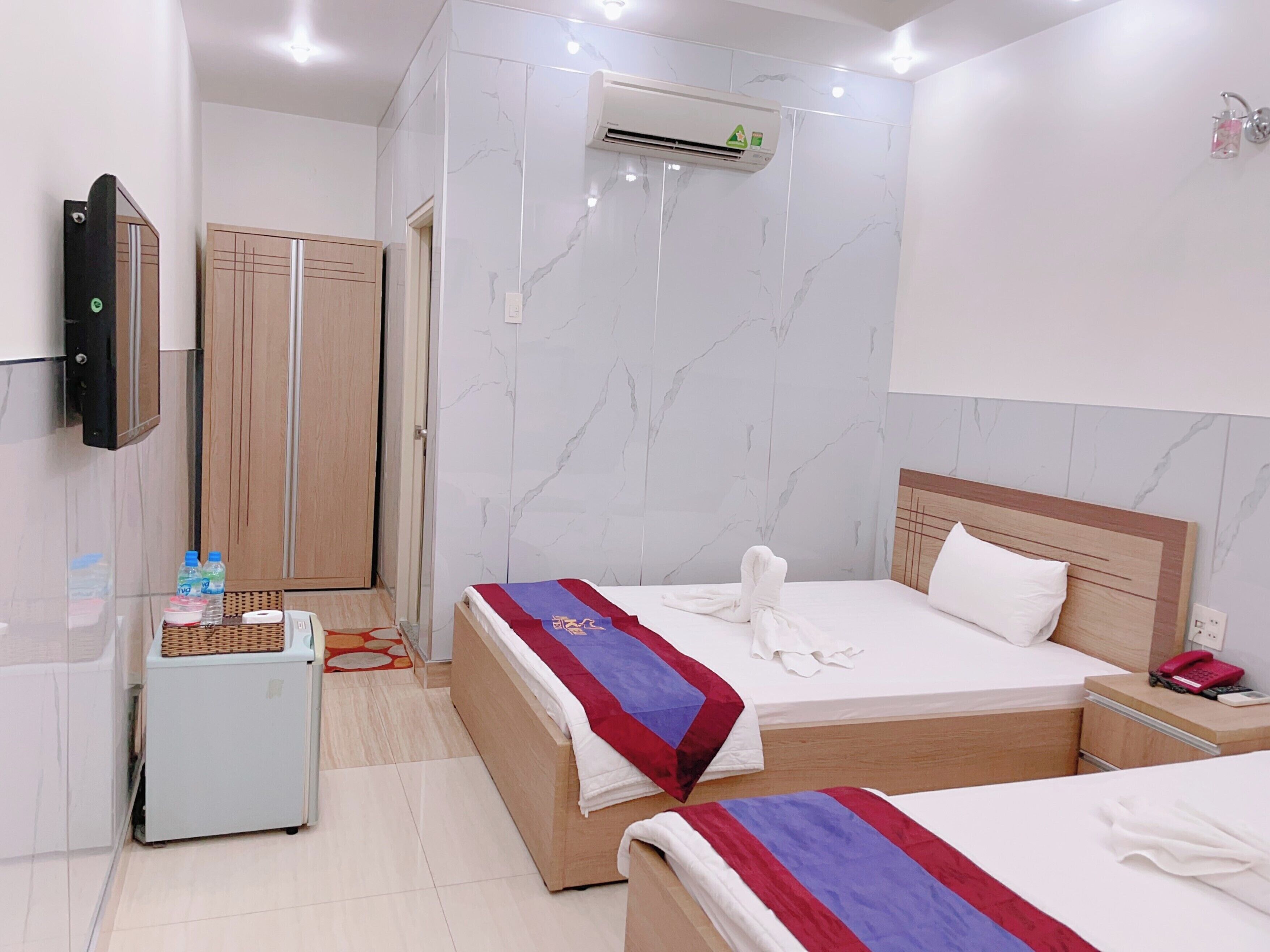 A hotel room with two beds, a minibar, a television, and an air conditioning unit.