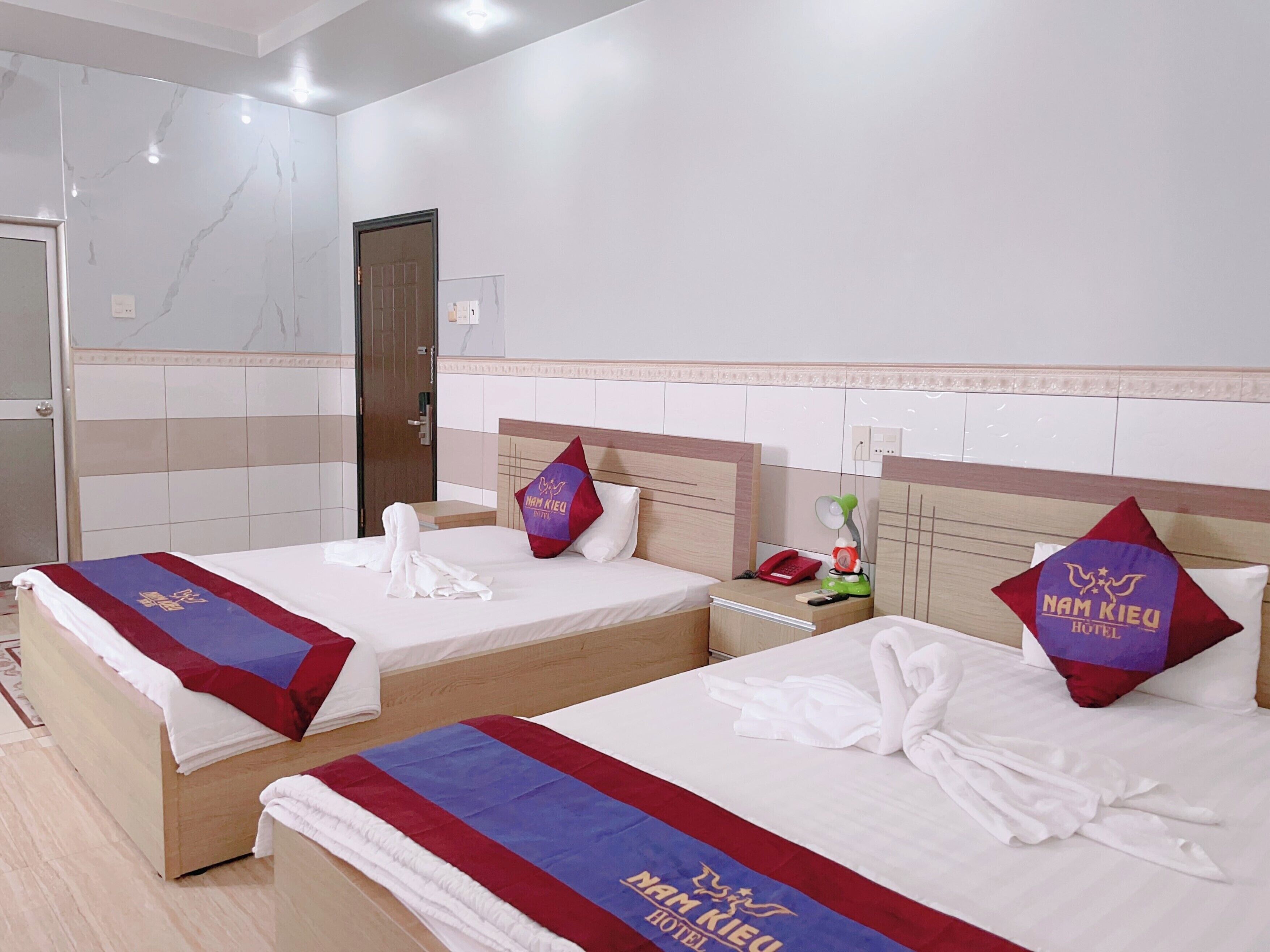 A hotel room with two beds, each with a red and blue bedspread, white linens, and matching pillows.
