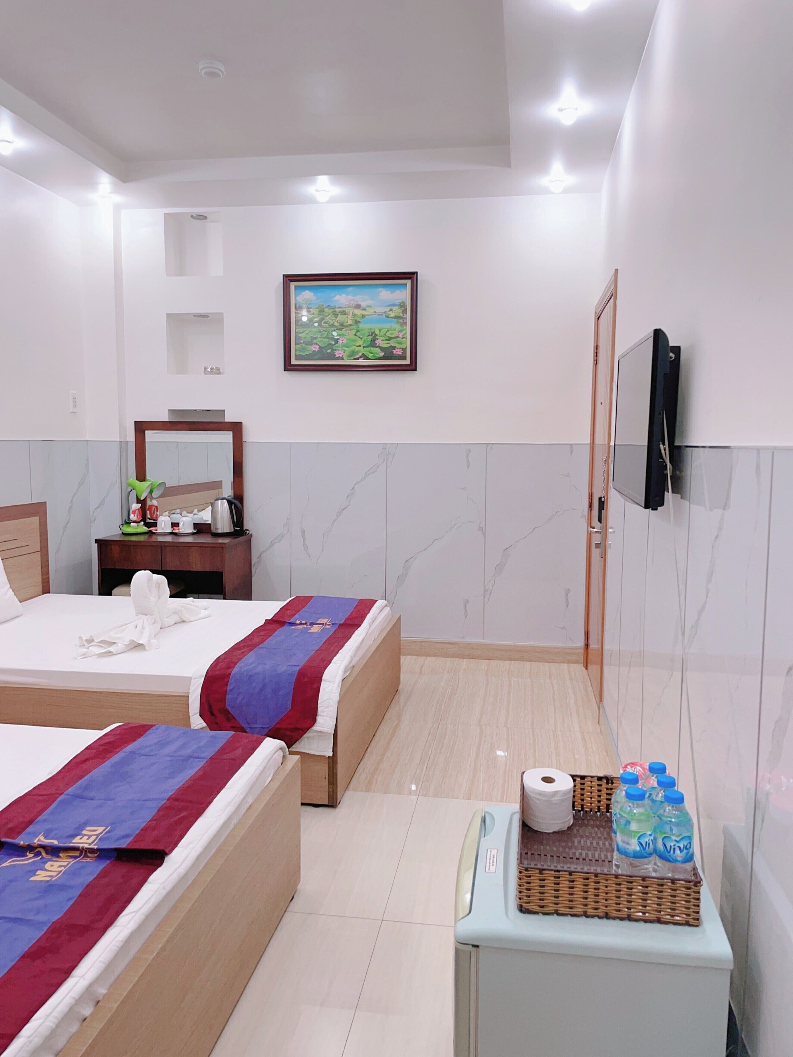 A hotel room with two beds, a television, a small table with toiletries, and a painting on the wall.