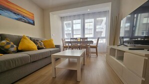 Un salon comprenant un canapé, une table basse, une table à manger avec des chaises et un téléviseur posé sur un meuble.