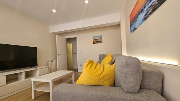 Un salon moderne avec un téléviseur à écran plat, un canapé avec des coussins, une table basse blanche et un tableau accroché au mur.