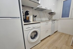 Une cuisine moderne équipée d’un lave-linge intégré, d’une machine à café et d’une fenêtre avec des stores.