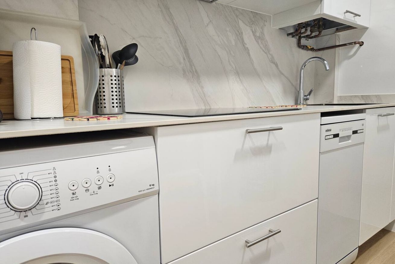 Une cuisine moderne équipée d’un lave-linge intégré, d’un évier et d’un pare-feu en marbre.