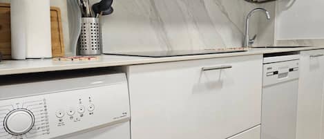 A modern kitchen with a built-in washing machine, a sink, and a marble backsplash.